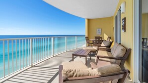 A balcony with a view of the ocean, furnished with chairs and a table, and a yellow wall with artwork. - Emerald Isle 1406 (Panama City Beach)
