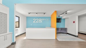 A modern interior with a reception desk, a wall displaying '228 SPACES', and a grey sofa. - Chic 1-bedroom Micro Studio Apartment (Cedar Falls)