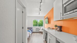 A modern kitchen with white cabinets, a microwave, and a window with a view of trees. - Chic 1-bedroom Micro Studio Apartment (Cedar Falls)