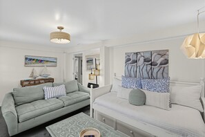 A modern living room with a sofa, a coffee table, and a bed with a patterned headboard. - Sand By Me | Dog-Friendly Ocean View, Edisto Beach (Edisto Island)