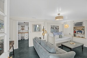 A modern living room with a sofa, a coffee table, and a dining area with a table and chairs. - Sand By Me | Dog-Friendly Ocean View, Edisto Beach (Edisto Island)