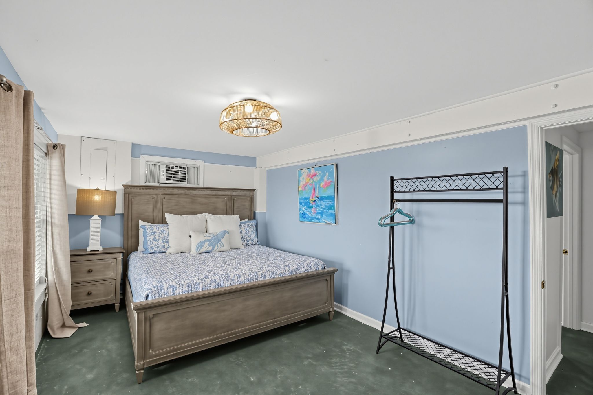 A bedroom with a bed, bedside table, lamp, air conditioning unit, and a wall-mounted artwork.
