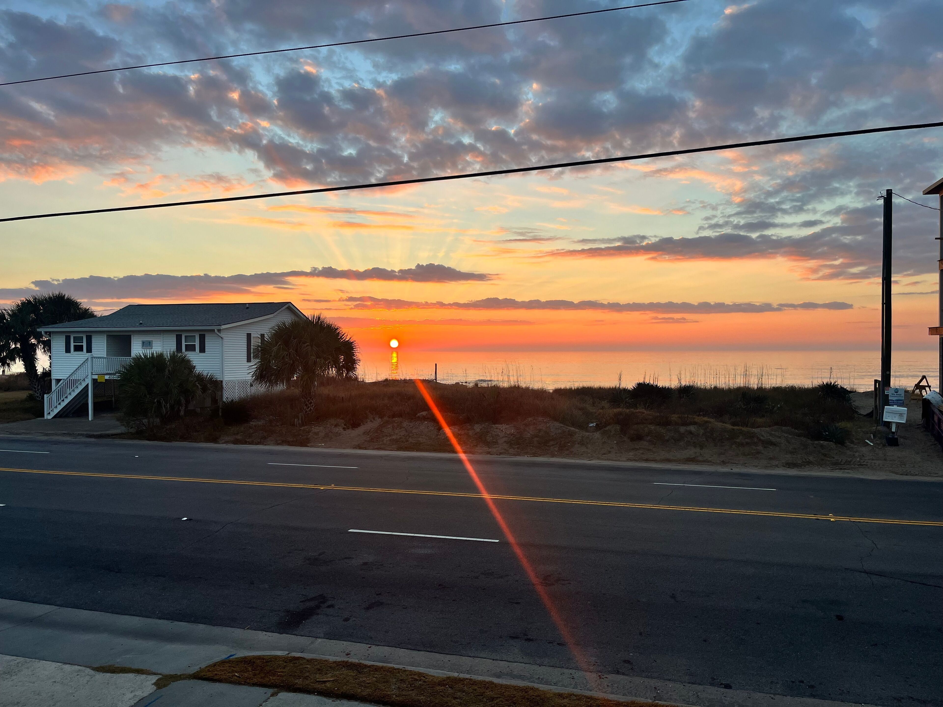 A coastal road with a house on the left and a beach on the right.