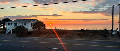 A coastal road with a house on the left and a beach on the right.