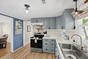A kitchen with grey cabinets, a stainless steel sink, and a black stove. - Sand By Me | Dog-Friendly Ocean View, Edisto Beach (Edisto Island)