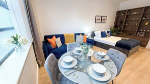 Una sala moderna con una mesa de comedor preparada para cuatro personas, un sofá, una cama y una estantería.