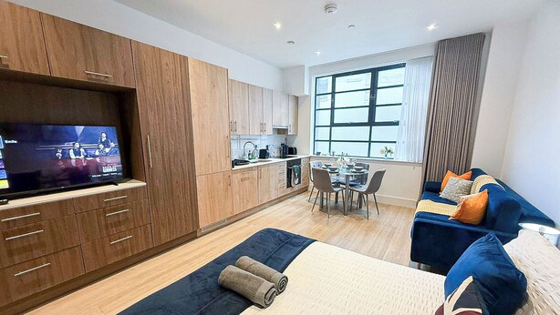 Un apartamento moderno con un televisor grande, una zona de comedor y una sala de estar acogedora con un sofá y cojines.