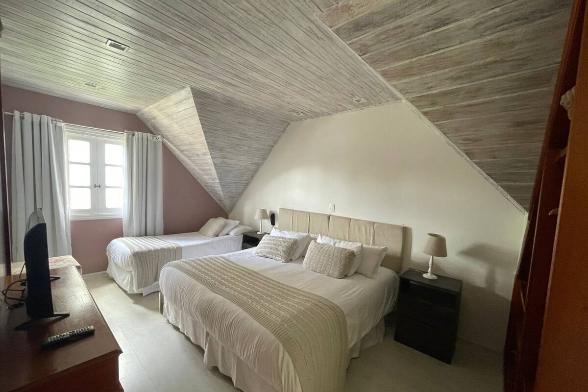A bedroom with two beds, a TV, and a window with curtains.