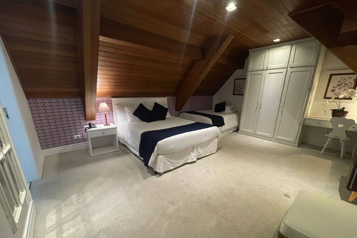 A bedroom with a large bed, a nightstand, a wardrobe, and a small desk with a chair.