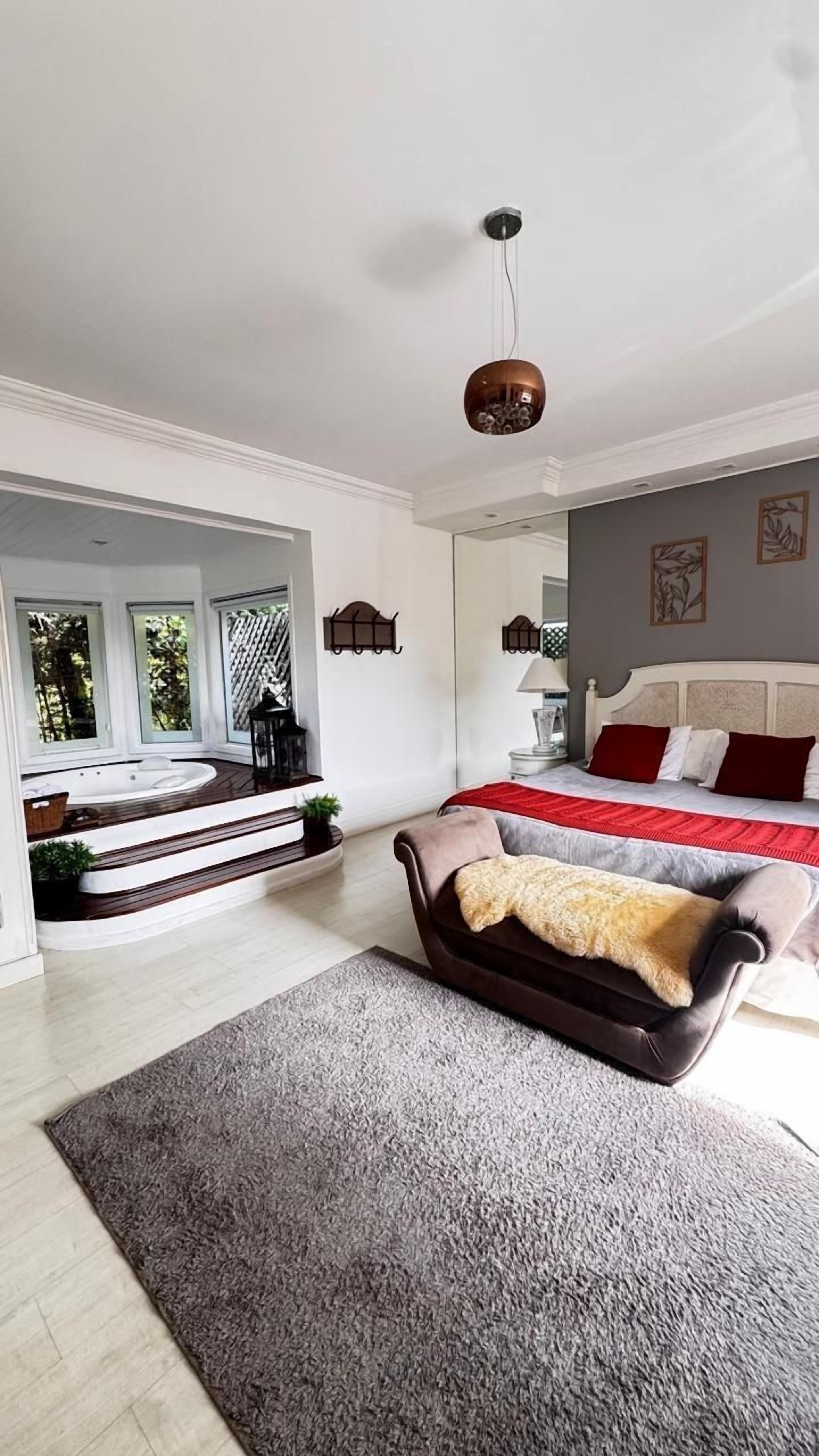 A modern bedroom with a large bed, a sitting area with a brown leather chair, and a view of a hot tub.
