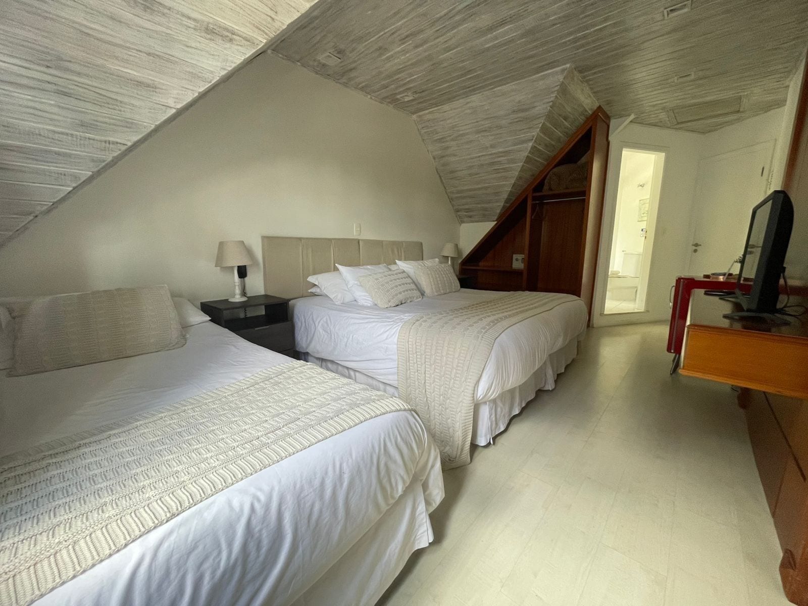 Une chambre avec deux lits, un bureau en bois et un plafond en pente.