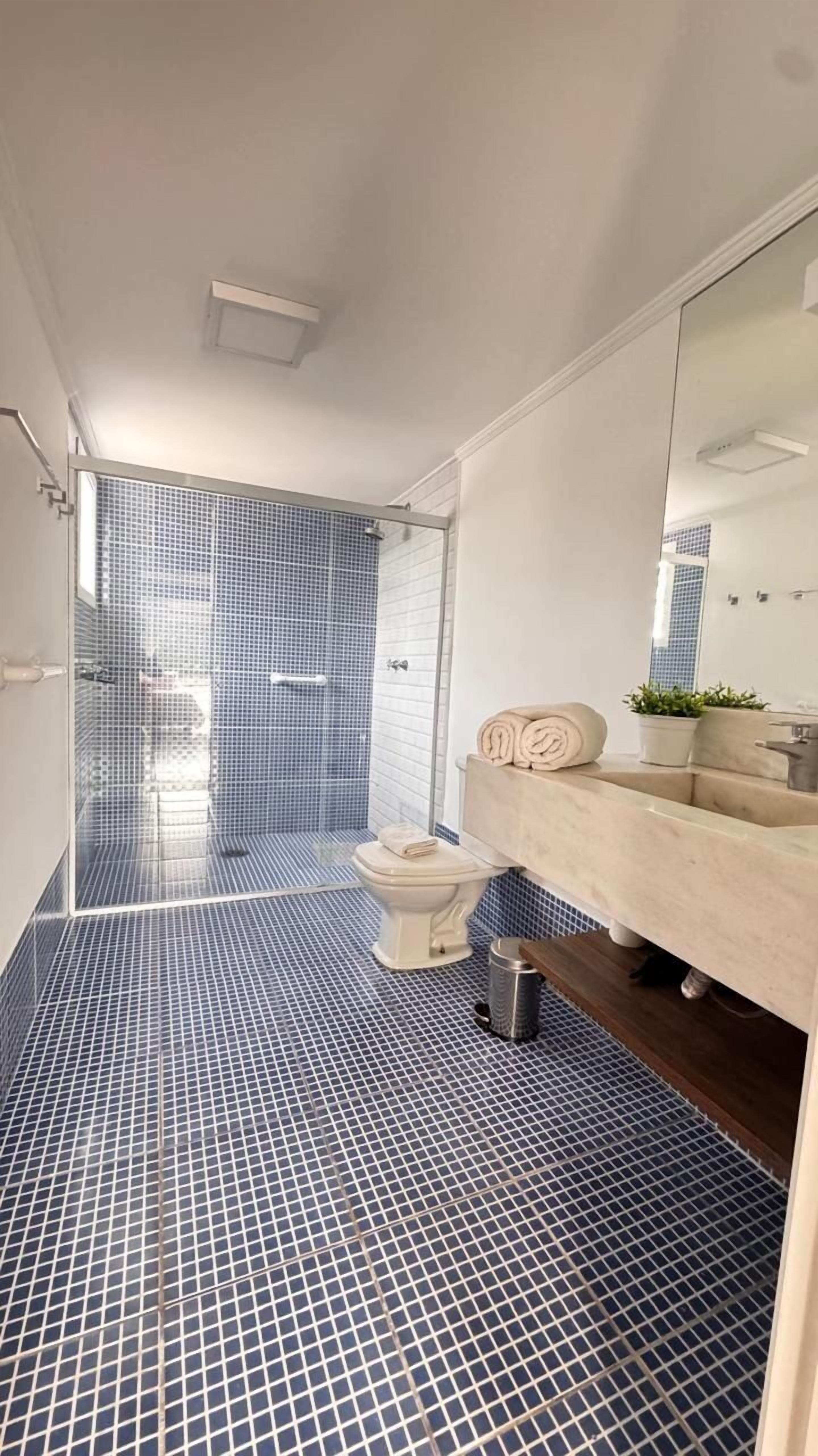 Un baño moderno con ducha revestida en azul, un inodoro blanco y un tocador color beige con espejo.