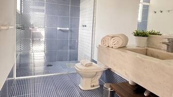 Un baño moderno con ducha revestida en azul, un inodoro blanco y un tocador color beige con espejo.