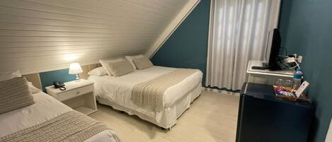 A bedroom with a sloped ceiling, a bed, a nightstand, a desk, and a television.