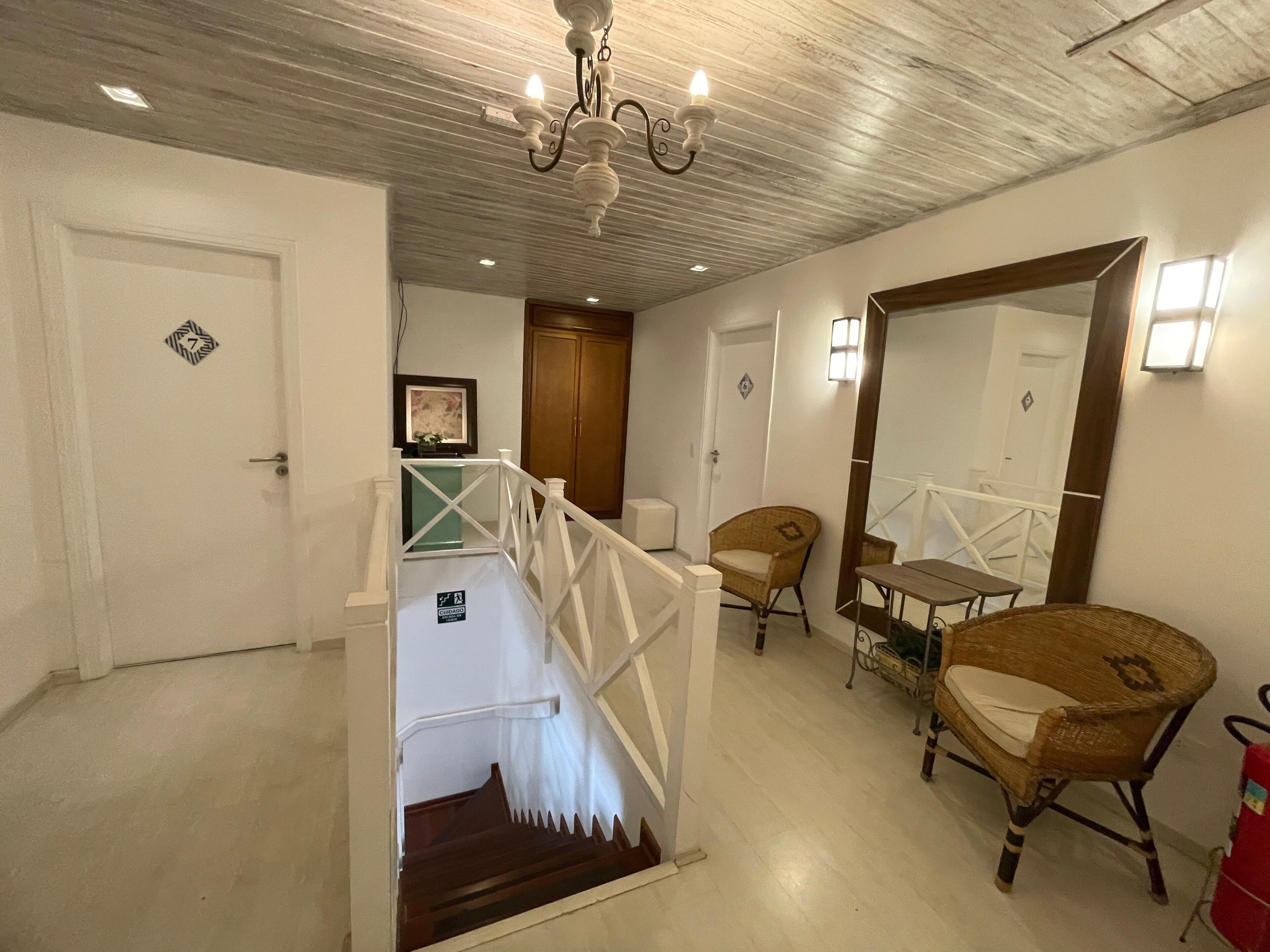 Un escalier avec une rampe blanche, une porte en bois, une chaise en osier, une petite table et un miroir.