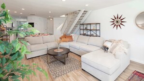 A modern living room with a light-colored sectional sofa, a round coffee table, and a staircase leading to an upper floor.