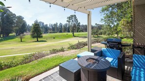 A covered patio area with outdoor furniture, a grill, and a view of a golf course.