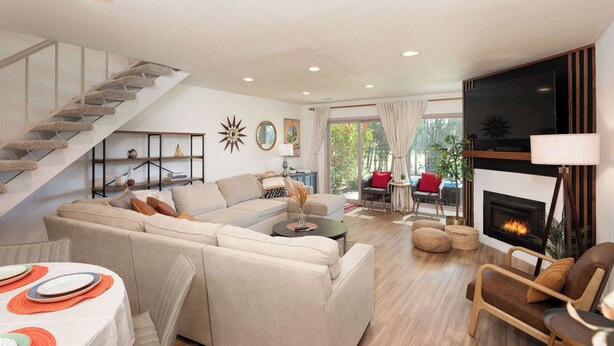A spacious living room with a staircase, a fireplace, and a large TV.