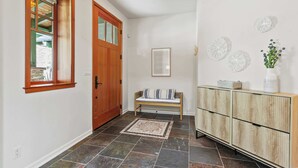 A hallway with a wooden door, a bench, a console table with decorative items, and a patterned rug. - Calm Coastal Retreat in Avila Beach (Avila Beach)