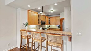 A kitchen with wooden cabinets, a granite countertop, and three wicker bar stools. - Calm Coastal Retreat in Avila Beach (Avila Beach)
