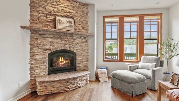 A living room with a stone fireplace, a comfortable gray armchair, and a large window with a view. - Calm Coastal Retreat in Avila Beach (Avila Beach)