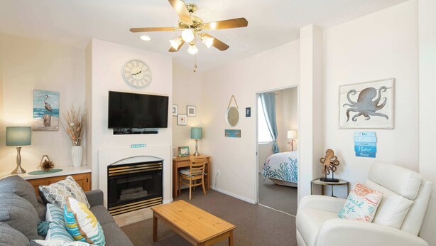 A living room with a sofa, a coffee table, a fireplace, a TV, and a ceiling fan. - After Dune Delight (Oceano)