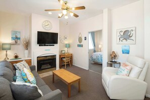 A living room with a sofa, a coffee table, a fireplace, a TV, and a ceiling fan. - After Dune Delight (Oceano)