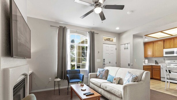 A living room with a sofa, a coffee table, a blue chair, a fireplace, and a kitchen in the background. - Eye Sea (Oceano)