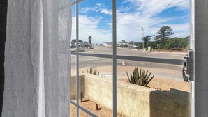 A view through a window with a metal grid, featuring a road, buildings, and a clear sky. - Eye Sea (Oceano)