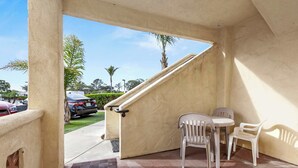 A covered outdoor seating area with a concrete floor, two white plastic chairs, and a small table. - The Seaside Sunshine (Oceano)