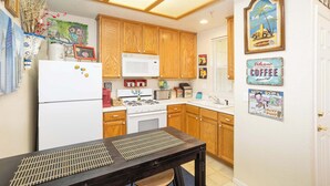 Une cuisine avec des meubles en bois, un réfrigérateur blanc, un four à micro-ondes, une cuisinière et un évier. Les murs sont décorés et il y a une table avec un set de table.