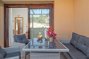 Ein Balkon mit Korbmöbeln, einem Glastisch und einer Vase mit Blumen.