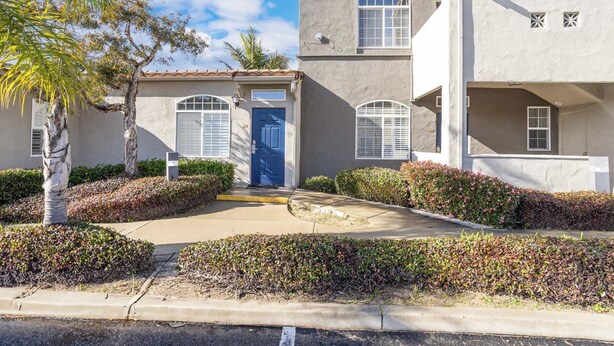 A two-story building with a blue door, white shutters, and a small balcony.