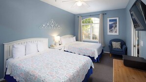 Ein Schlafzimmer mit zwei Betten, einem Deckenventilator, einem Nachttisch mit Lampe, einem Sessel und einem Fenster mit Vorhängen.