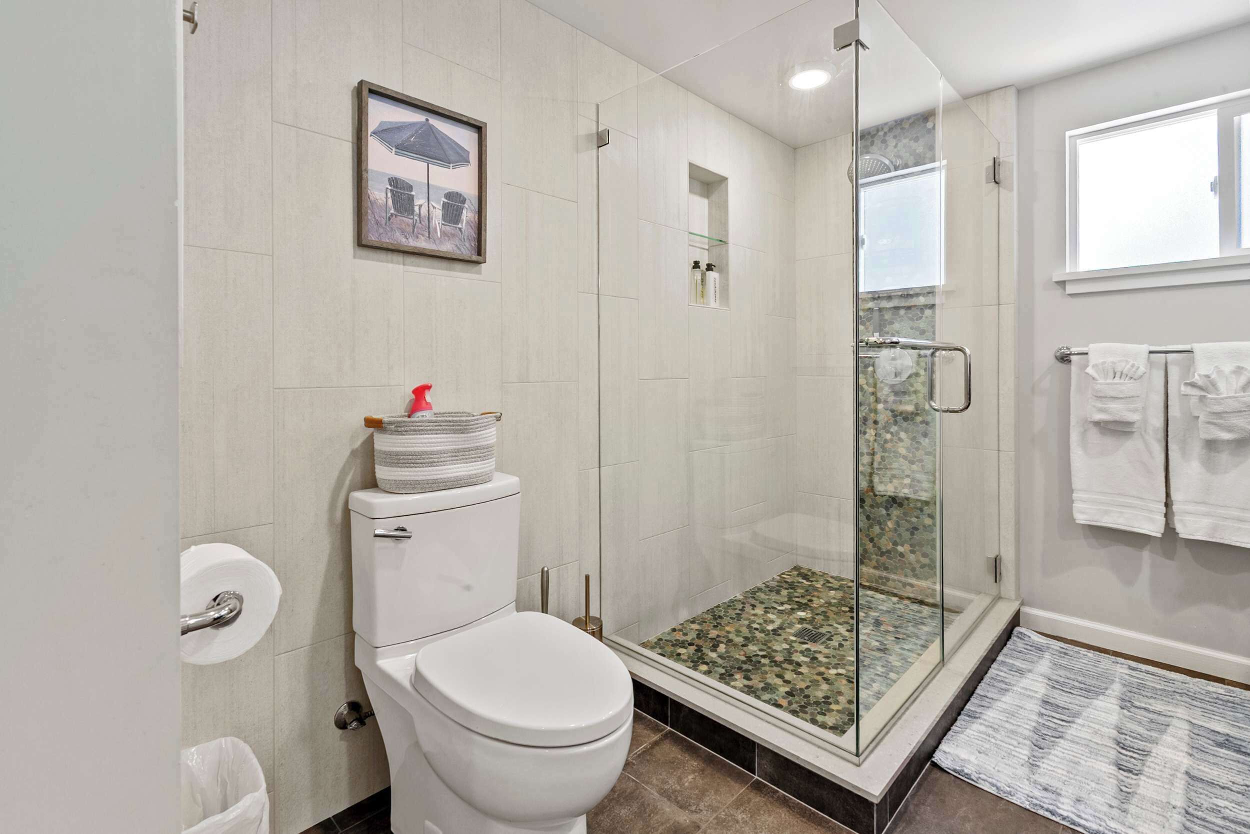 A bathroom with a toilet, a glass shower enclosure, and a small shelf with toiletries.