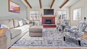 A living room with a fireplace, a sofa, an ottoman, patterned chairs, and a large painting on the wall. - The Bay Escape (Baywood-Los Osos)