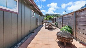 A narrow outdoor pathway with a patio table and chairs, a barbecue grill, and a wooden fence on one side. - The Bay Escape (Baywood-Los Osos)