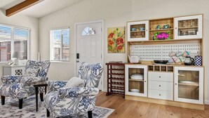 A living room with two patterned armchairs, a wooden cabinet with glass doors, and a painting on the wall. - The Bay Escape (Baywood-Los Osos)