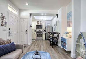 A modern kitchen with white cabinets, stainless steel appliances, and a dining area with a blue cabinet and a chandelier. - The Seaside Sanctuary (Oceano)