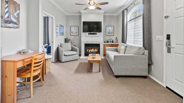 A living room with a fireplace, a ceiling fan, a TV, and a sofa. - Coastal Cutie (Oceano)