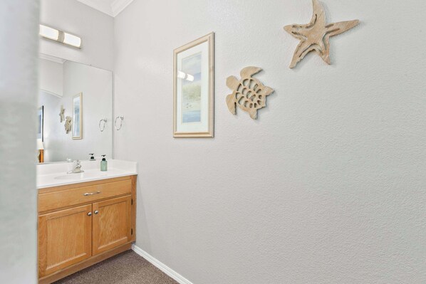Un baño con tocador de madera, un cuadro enmarcado y estrellas de mar decorativas en la pared.