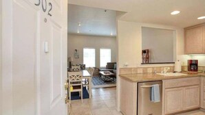 Et moderne køkken med indbygget ovn og vask, et spiseområde med bord og stole, samt en stue med sofa og sofabord.