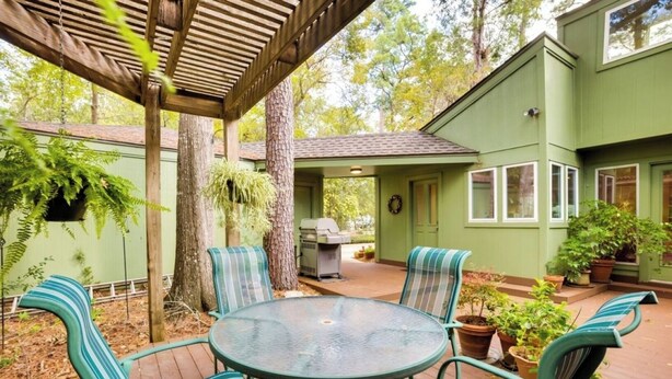 A patio with a round table and striped chairs, surrounded by potted plants and trees. - Woodlands Escape: 3BR Texas Retreat w/ Forest View (The Woodlands)