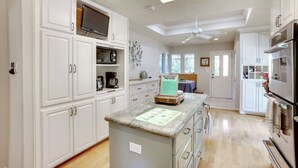 A spacious kitchen with white cabinets, a granite countertop, a built-in TV, and a ceiling fan. - Woodlands Escape: 3BR Texas Retreat w/ Forest View (The Woodlands)