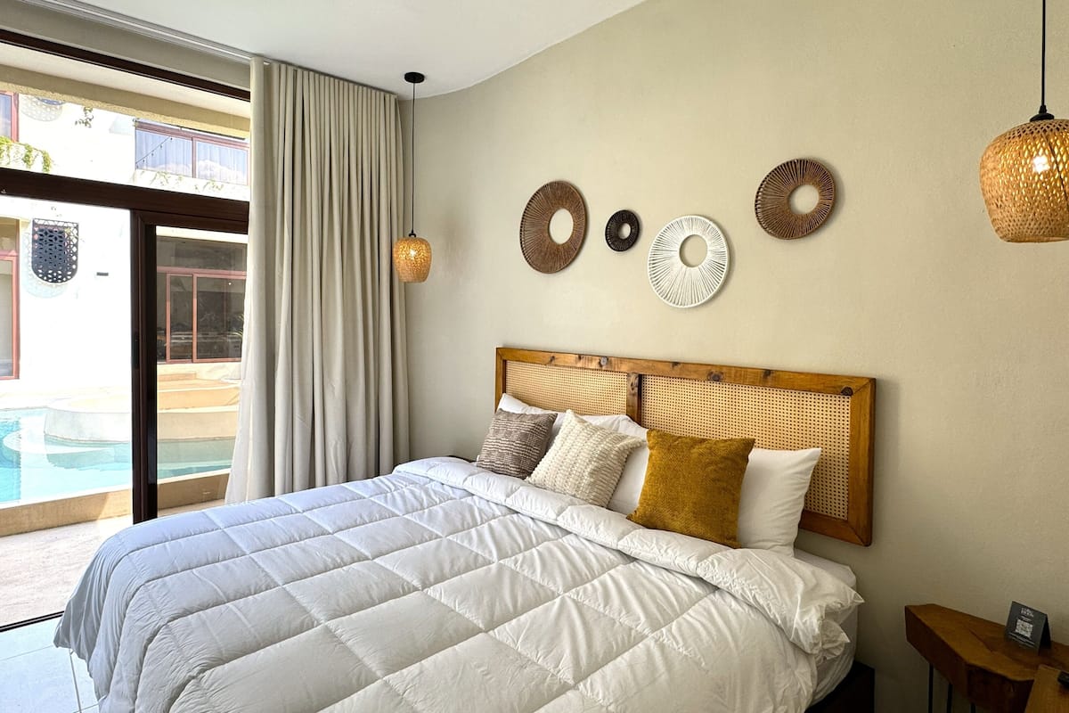 A bedroom with a large bed, a wooden headboard, and a view of a swimming pool through a glass door.