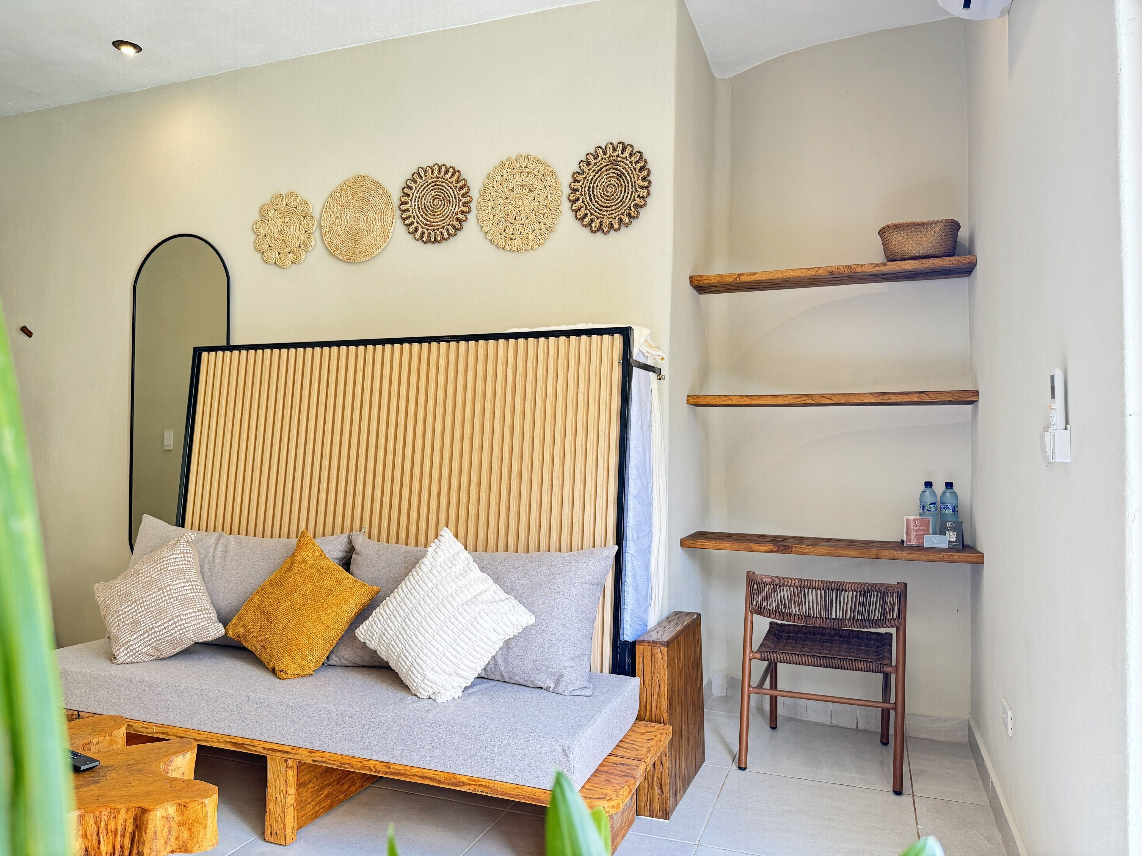 Une chambre moderne avec un canapé-lit, des tables de chevet en bois, un fauteuil en osier et des œuvres d’art décoratives au mur.