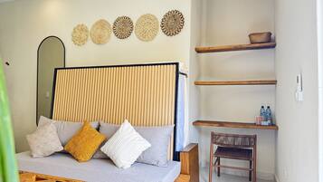 A modern bedroom with a sofa bed, wooden side tables, a woven chair, and decorative wall art.
