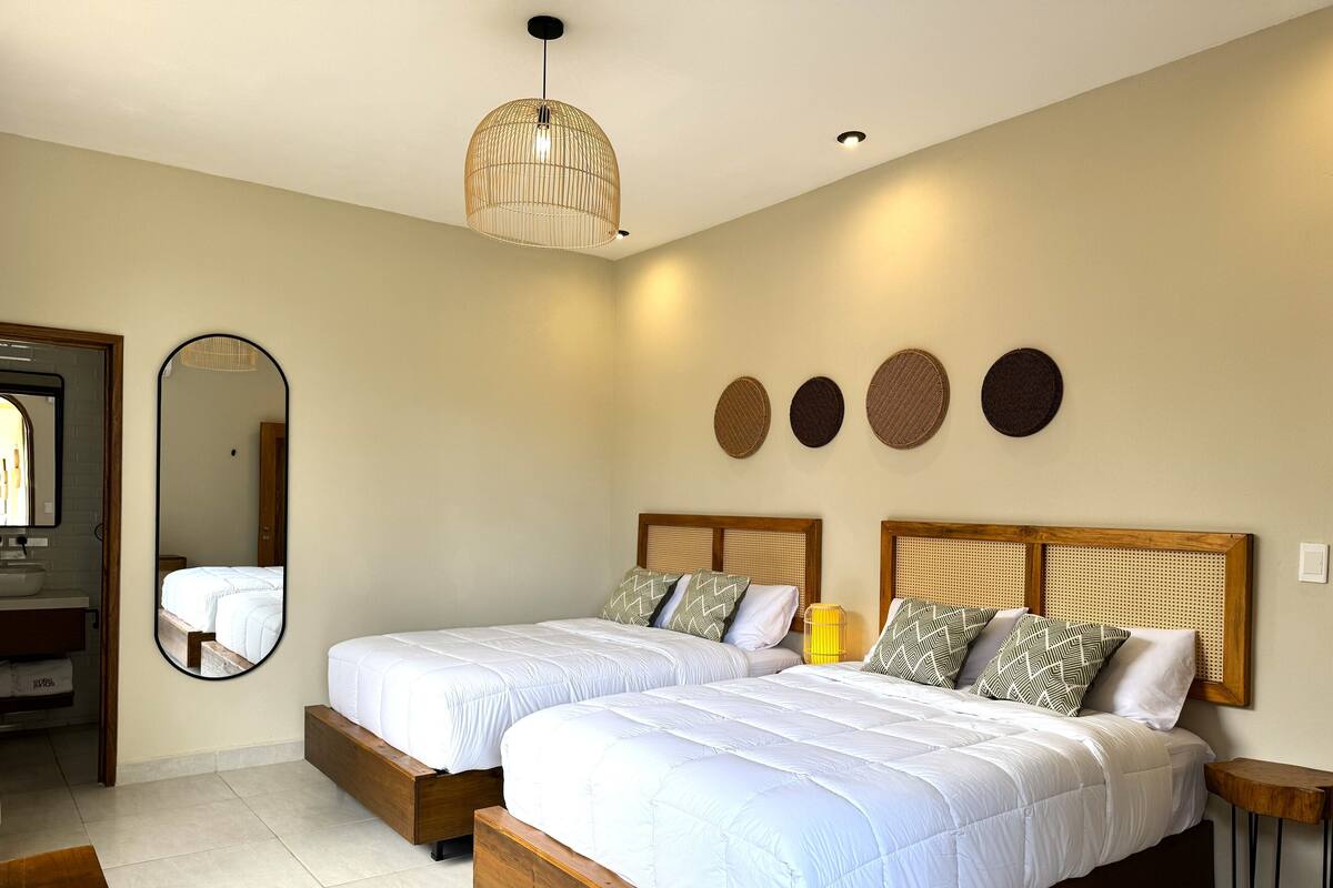 A bedroom with two beds, a large mirror, and a ceiling light fixture.