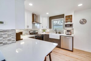 Una cocina moderna con armarios blancos, una campana extractora de acero inoxidable, horno empotrado, microondas y lavavajillas.