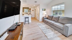 Uma sala de estar moderna com um sofá cinzento, mesa de centro de madeira e uma área de cozinha ao fundo.